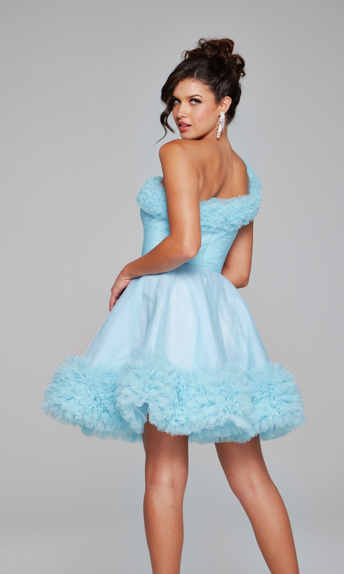 A woman poses in the Jovani 39665 One-Shoulder Short Ruffle Hoco Dress, featuring light blue fabric, a flared skirt, and ruffled trim.